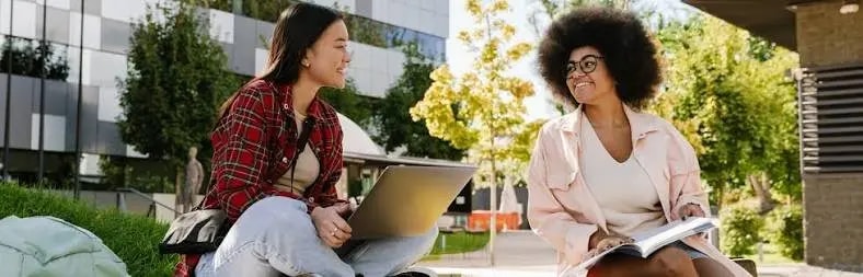 Two students studying outdoors with a laptop and notes
